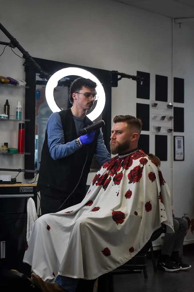 A barber at The Garage blow-drying a client's fresh fade under a ring light